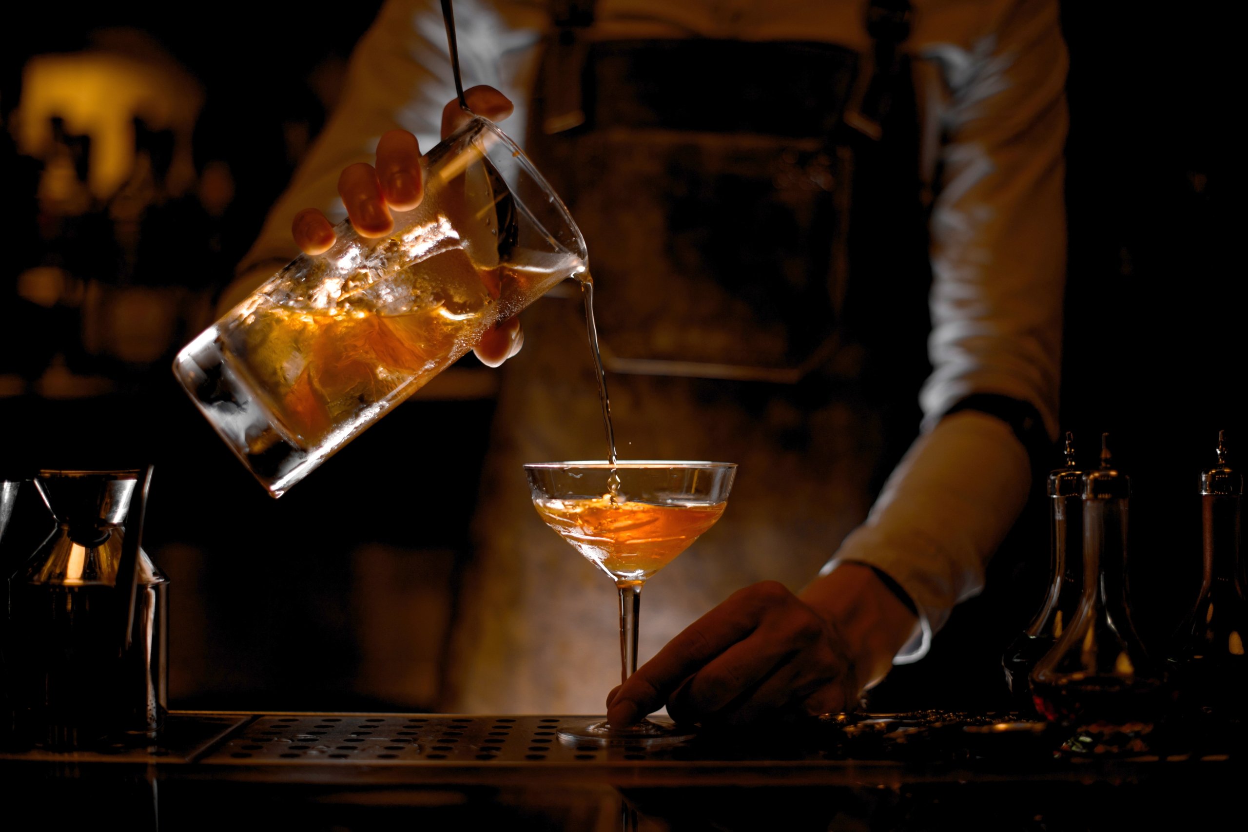 bartender pouring a cocktail into a glass